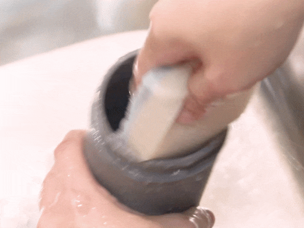Close up image of hands in yellow protective rubber gloves washing white cup under running tap water